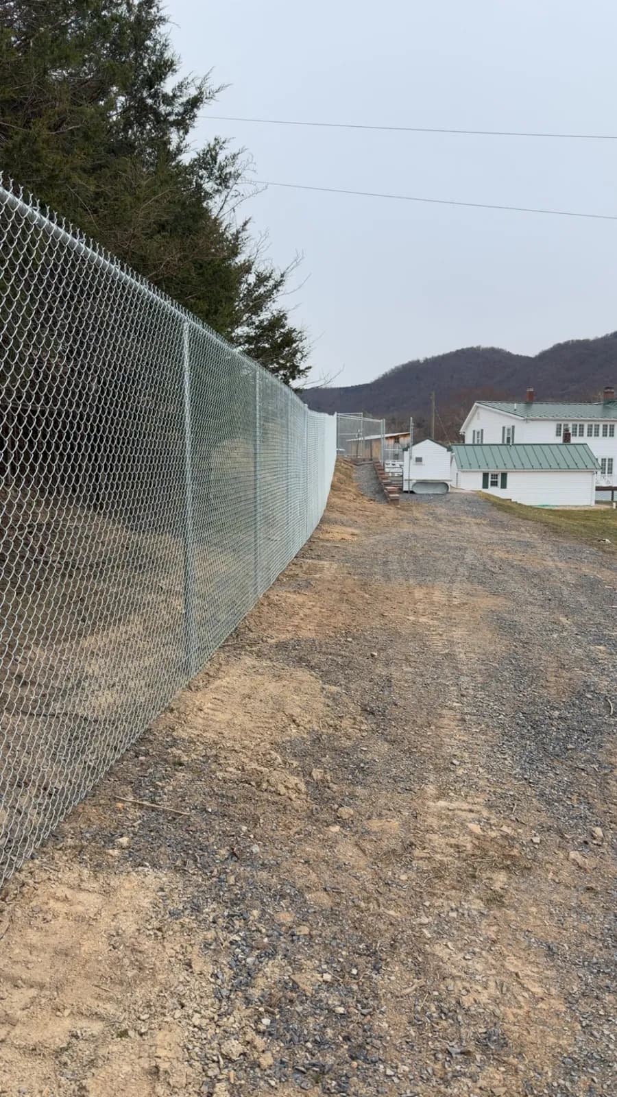 Tall galvanized chain-link security fence line along a gravel drive