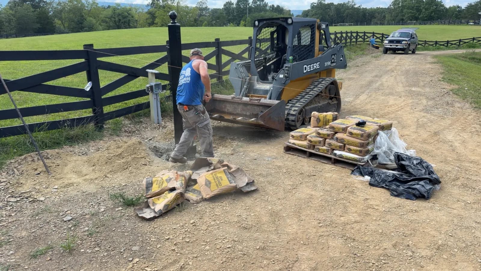 Crew member in an Allied Fence & Decks shirt unloading concrete beside a skid steer on a board-fence job