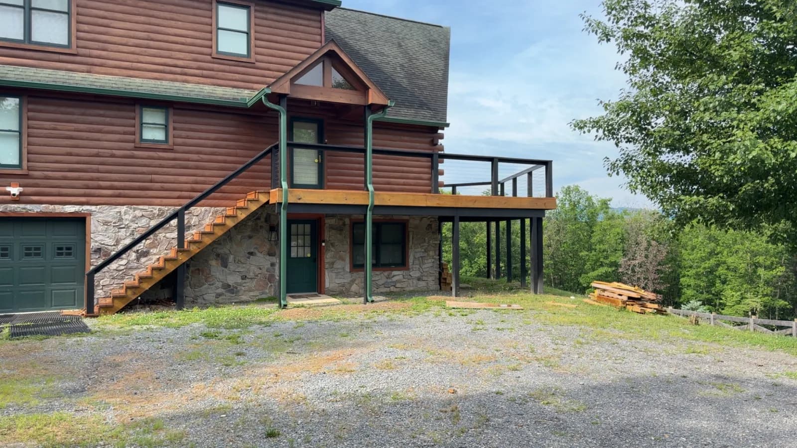 Stained deck and stairs wrapping a timber lodge on a stone foundation