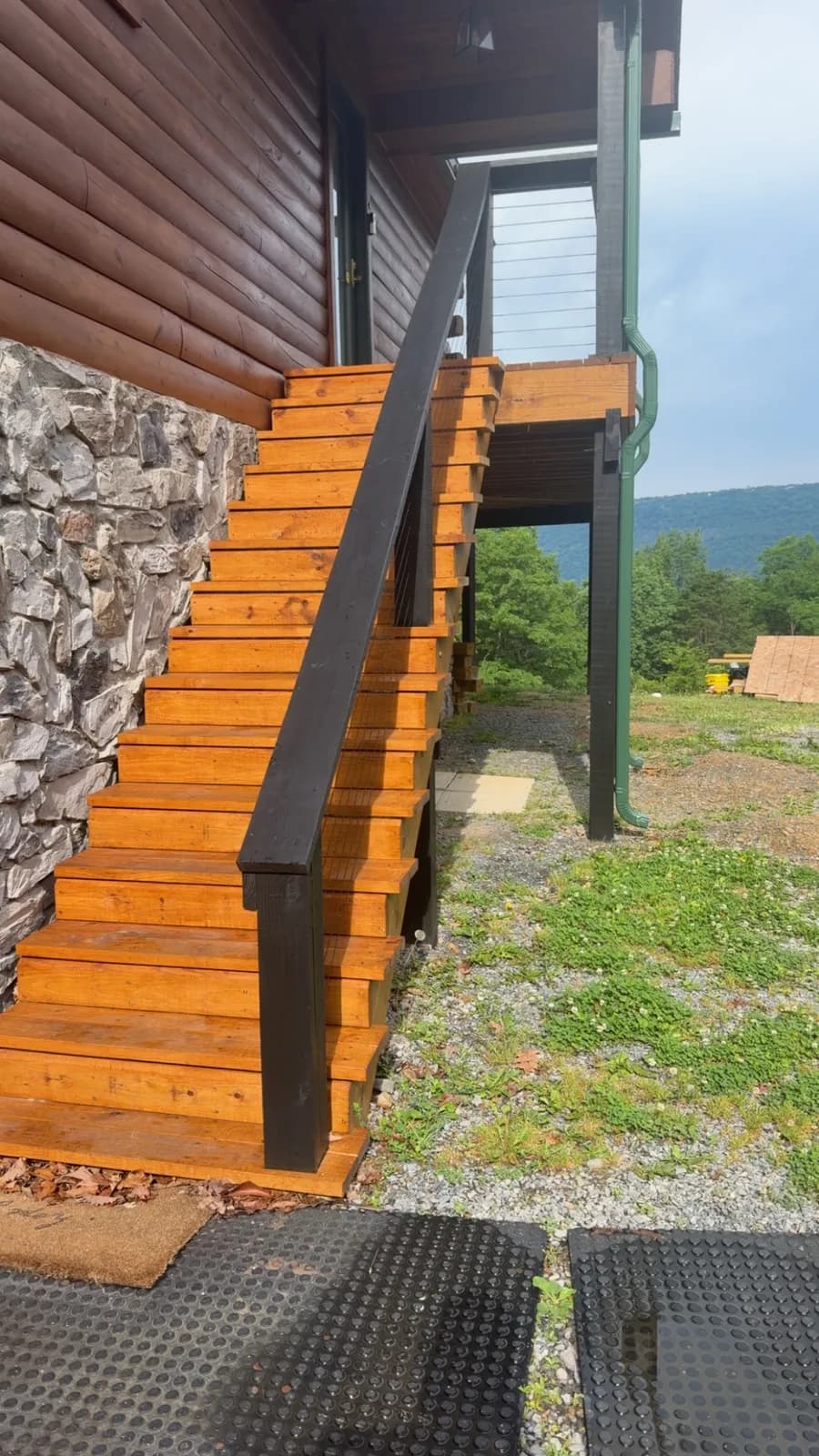 Freshly stained wood stairs with black handrail beside a stone foundation