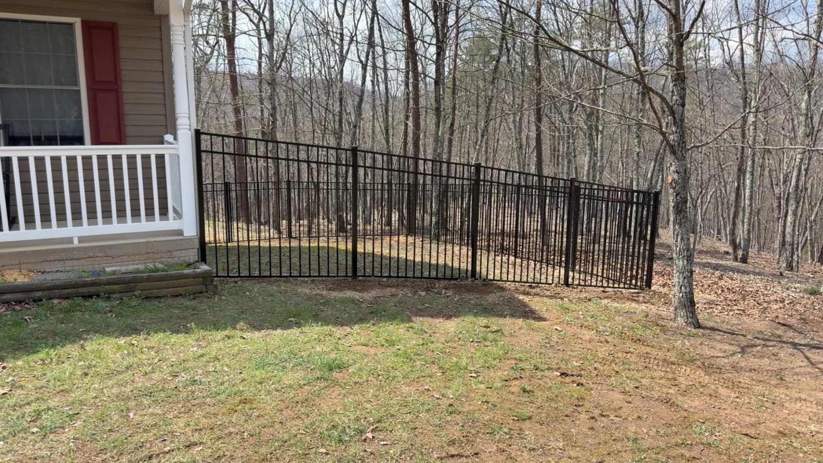 Black ornamental metal fence line along a wooded backyard