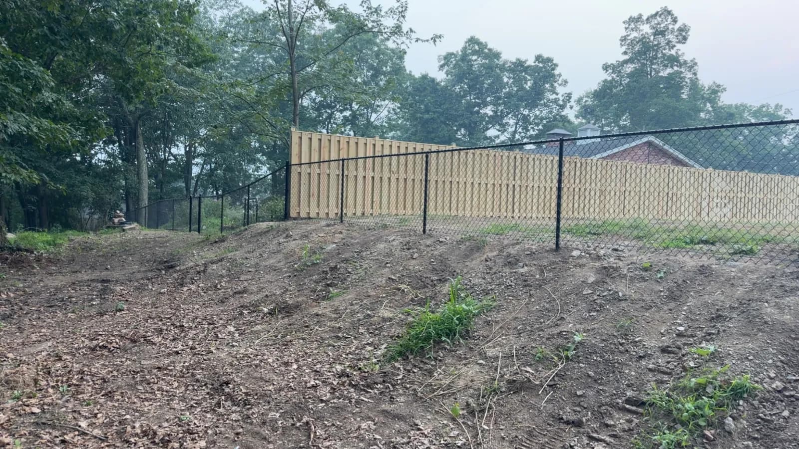 New vertical-board wood fence with black chain-link yard fencing